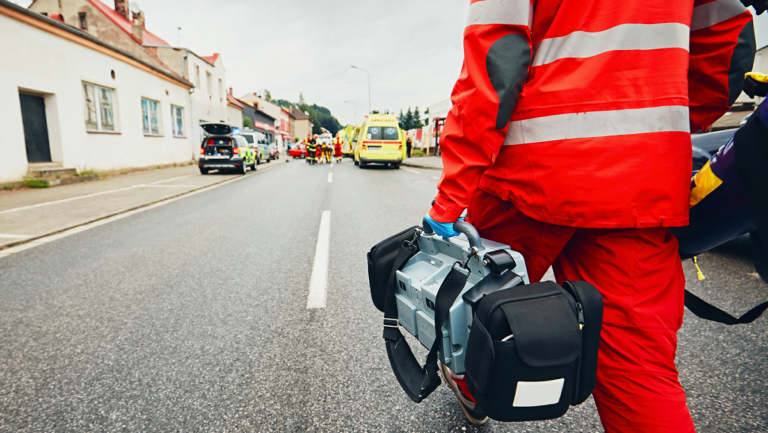 Ensihoitaja kävelemässä onnettomuuspaikalle defibrillaattorimonitori kädessään.